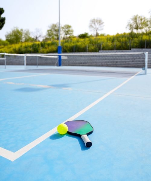 A pickleball paddle and ball rest on a blue court, poised for the next serve. Concept of anticipation and readiness in sports.